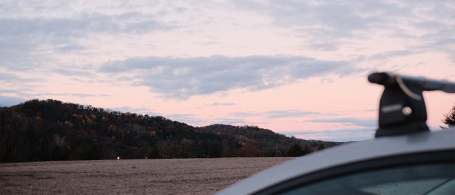 Soft fog hanging low over rolling fields at dawn, with the first warm light breaking on the horizon.
